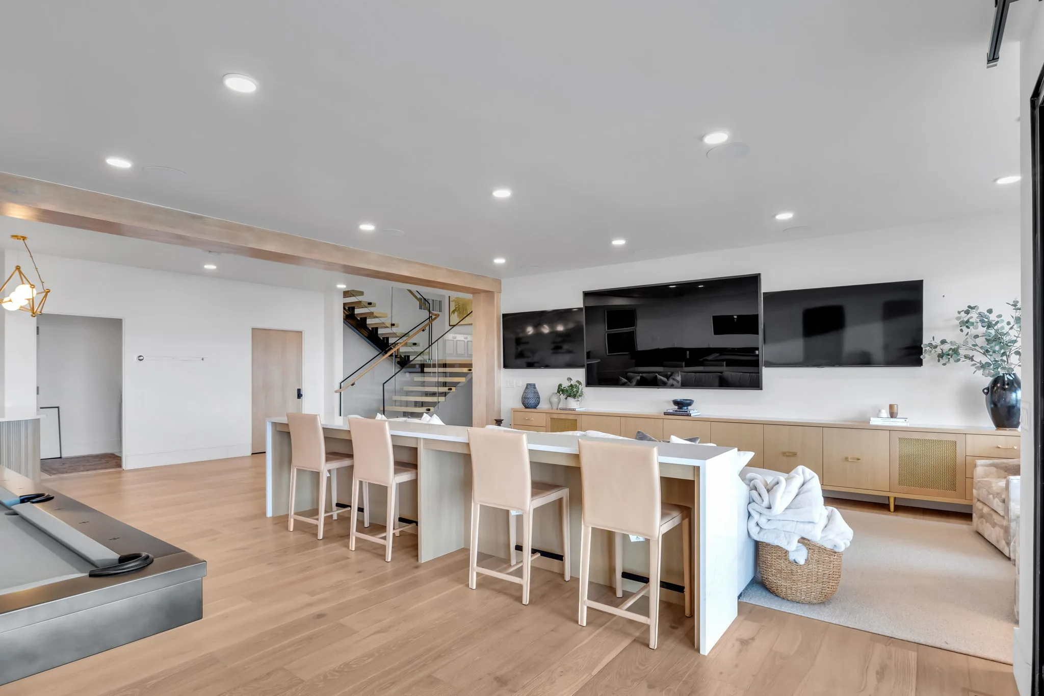 Custom home lower-level entertainment room with bar seating, multiple TVs, and floating staircase by Bird