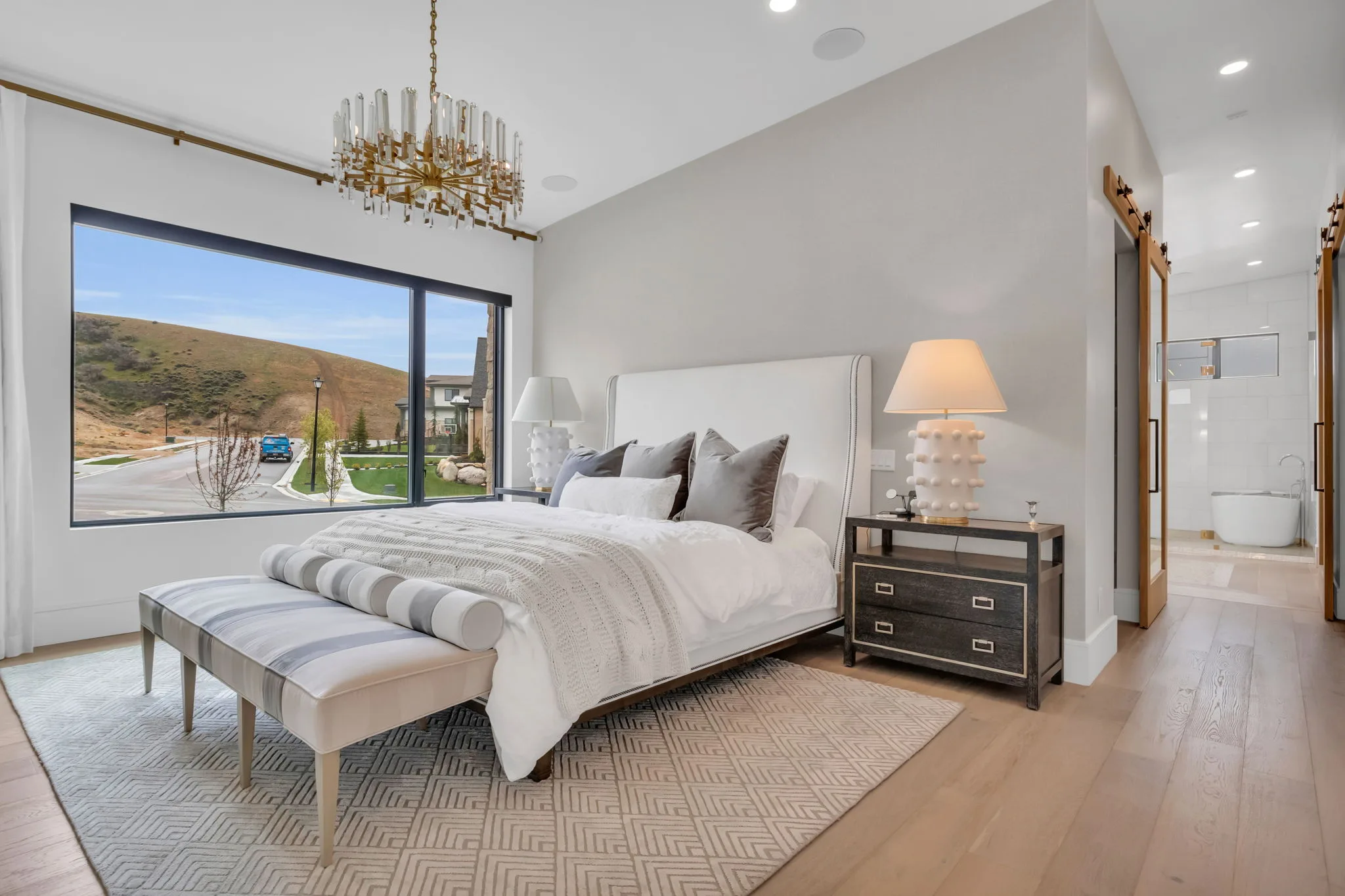 Custom primary bedroom suite with large picture window and crystal chandelier in a Bird-built Utah home